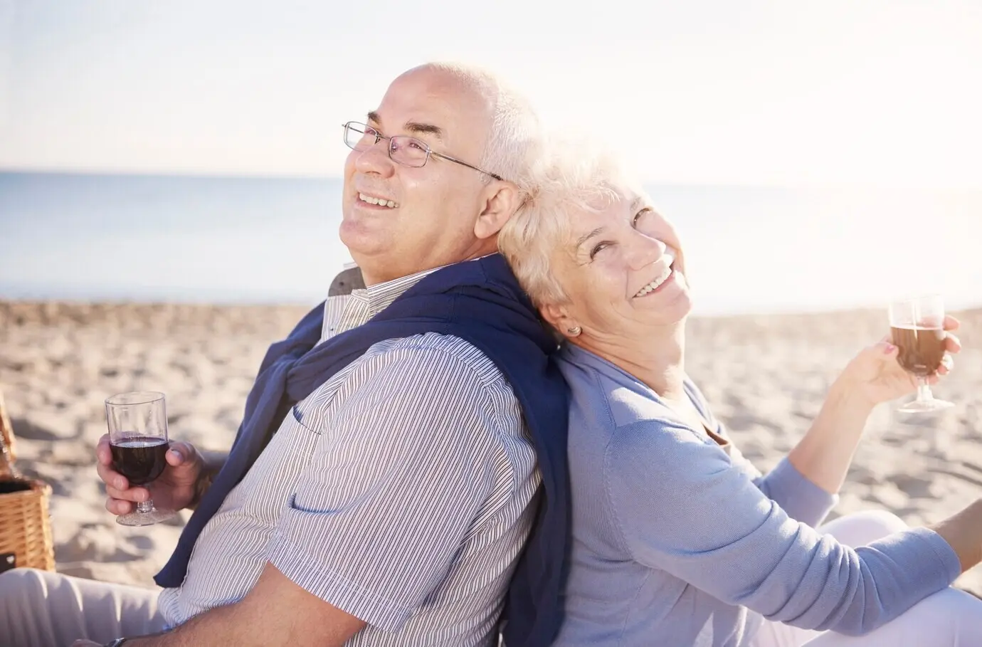 Senioren sitzen Rücken an Rücken und trinken Wein. Seniorenpaar am Strand, Konzept für Ruhestand und Sommerurlaub.